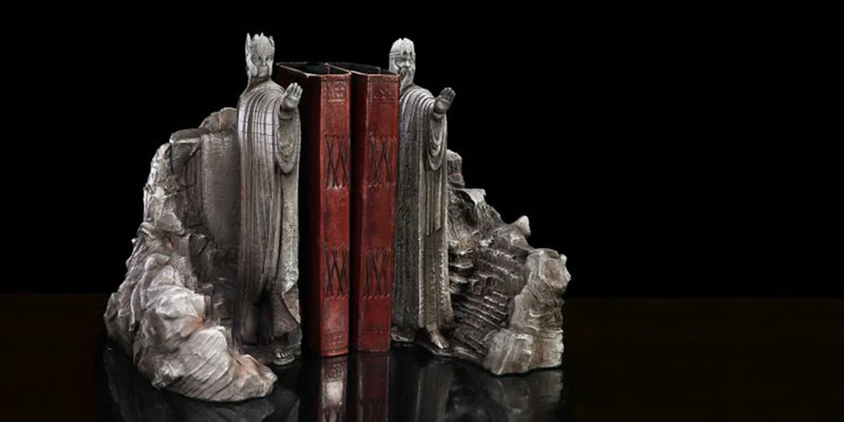 A pair of ornate bookends shaped like classical robed figures standing on rocky bases, holding upright red books between them, photographed against a black background.