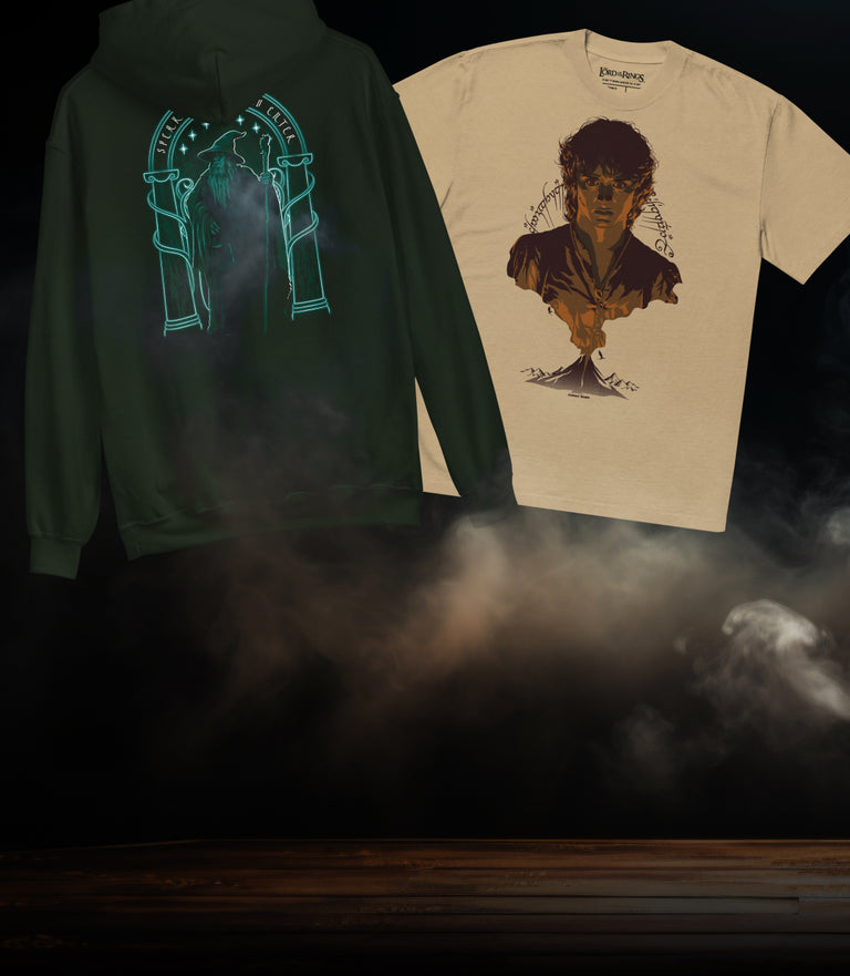 A dark green hoodie and a cream t-shirt displayed side-by-side against a dark, smoky background. The hoodie features a glowing cyan graphic of two pillars on the back, while the t-shirt displays a graphic of a face emerging from a tree trunk.