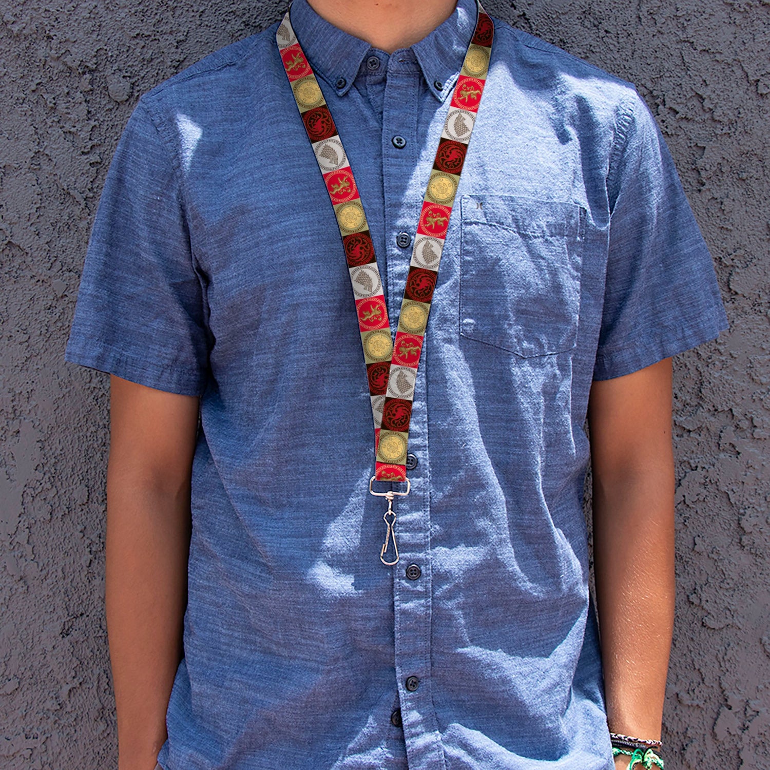 Person in a blue short-sleeve shirt wears a colorful lanyard with patterned circles, against a dark textured wall. Arms visib